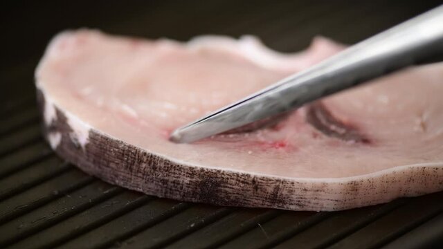 Swordfish Xiphais gladius steak portion putting on a grill pan. Moving and flipping with cooking tongs