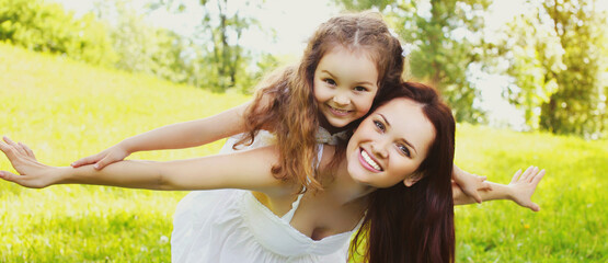 Portrait of beautiful happy smiling mother with little girl child having fun in a summer park