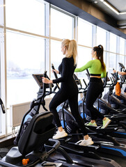 Fototapeta na wymiar Athletic woman doing fitness cardio exercises in the gym on stepper machine. Two sporty women working out together