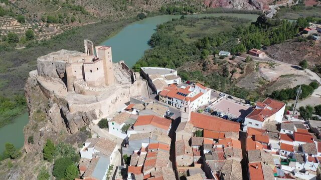 Scenic aerial view of medieval Cofrentes Castle towering over city residential buildings atop rocky cliff over Cabriel River, Valencia, Spain. High quality 4k footage