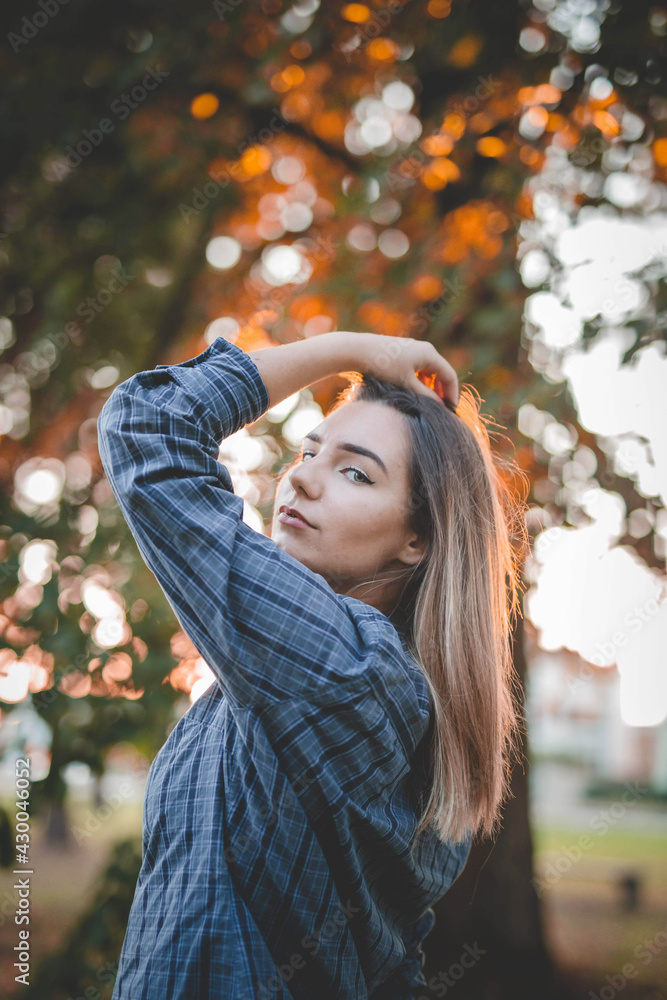 Poster beautiful green-eyed woman wearing a checkered green shirt posing in the park during sunset