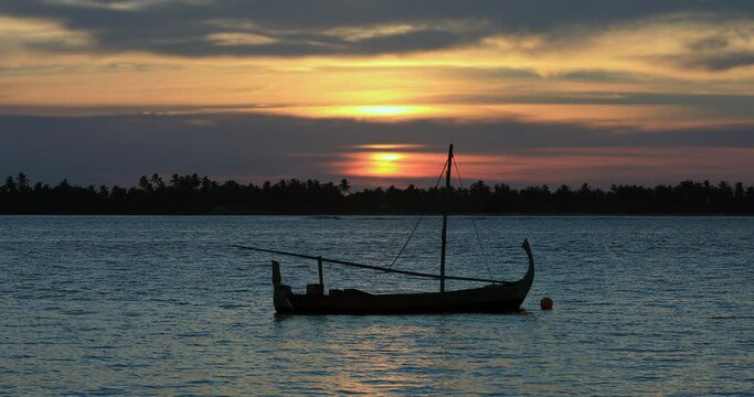 Sunset in Maldives with silhouette of sailboat dhoni. Dramatic palm trees and ocean waves, vacation, tourism holiday island for background graphics