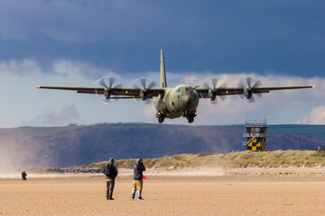 A Royal Air Force C-130 performing tactical landings and takeoffs from the public beach at Cefn Sidan Sands in West Wales. - obrazy, fototapety, plakaty