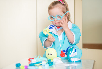 Down syndrome in a little girl, a child in a doctor's costume playing with a doll and with medical...