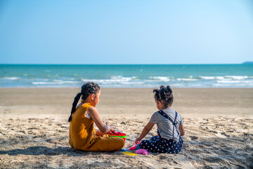 Happy family on summer vacation. Two little Asian girl sibling sit on sand beach play beach toys together with happiness. Two child girl kid enjoy and having fun outdoor activity lifestyle in summer.