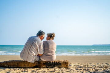 Happy Asian family on beach travel vacation. Senior couple sitting on the beach and talking together with happiness. Healthy elderly husband and wife relax and enjoy summer outdoor lifestyle activity.