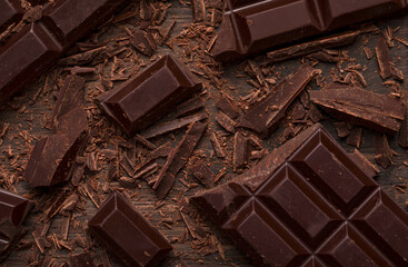 Grated and chopped dark chocolate bar pieces on a dark wood background