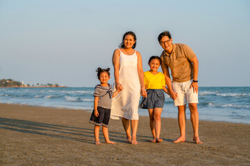 Portrait of Happy family on summer holiday vacation. Asian couple with two child girl kid holding hands and walking together on tropical beach. Family enjoy and having fun outdoor lifestyle in summer.