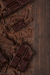 Grated and schopped pieces of dark chocolate bar on a dark wooden background