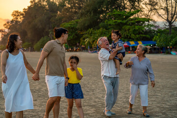 Fototapeta premium Happy big Asian family on beach holiday vacation. Multi-generation family holding hands and walking together on tropical beach at summer sunset. Family enjoy and having fun outdoor activity lifestyle.