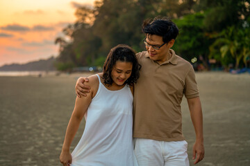 Happy Asian family on beach travel vacation. Adult couple holding hand and walking together on the beach at summer sunset. Smiling husband and wife relax and enjoy romantic outdoor lifestyle activity