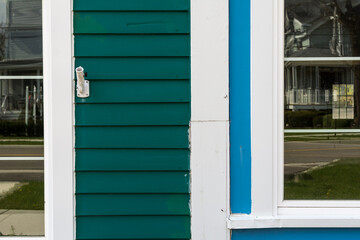 Fototapeta premium Old wooden storefronts side by side one green and one blue both with white trim; reflections in the windows of a small town