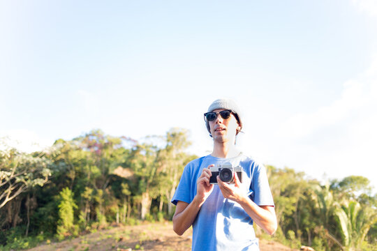 Portrait of a young man holding a photo camera and taking pictures outdoors.