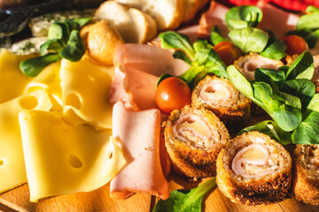 Close up on cheese and ham rolls on the wooden board plate with various food and cheese ready to eat - appetizer on the table full frame