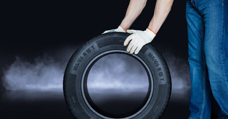 Mechanic holds a tire on creative black background. Tire changing concept