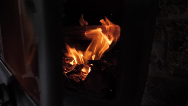 Hand opening metal door of small cabin fireplace as red hot fire burns wood and sticks with slow motion flames flickering with ember and sparks flying up.