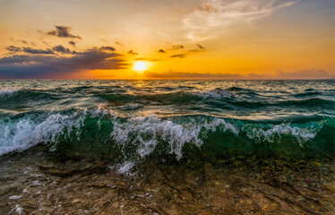 A Wave is Crashing to the Seashore as the Sun Sets in in the Colorful Sunset Sky