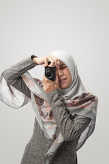 portrait of a moslem woman ooks through the viewfinder while shooting with the camera isolated in white background.