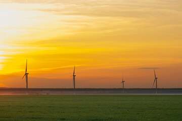 Fototapeta na wymiar many windmills stand on a large field spinning in the evening against a sunset orange sky. Alternative Energy Concept