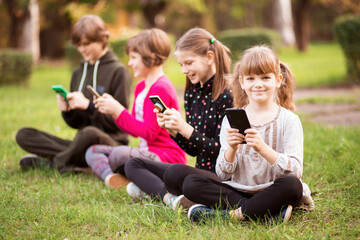 Outdoor portrait of little girls and boys playing with phones . High quality photo