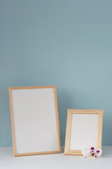 Spring still life. Two wooden portrait frames mockup on white table with orchid flower. Blue wall background.