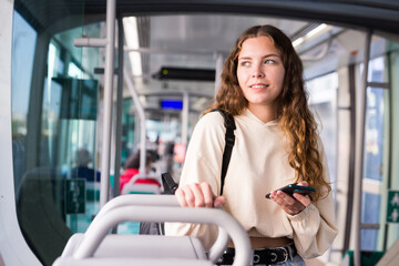 Fototapeta na wymiar Portrait of a positive girl traveling in public transport and texting on a mobile phone with friends