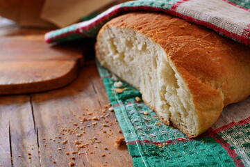 fresh baked loaf of bread cut with white crumb and crispy fried crust on a wooden table under a...
