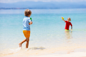 Child with toy water gun. Kids vacation beach fun.