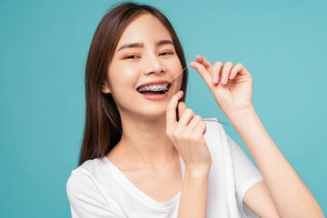 Young Asian woman cleaning braces on teeth with dental floss on blue background, Concept oral...