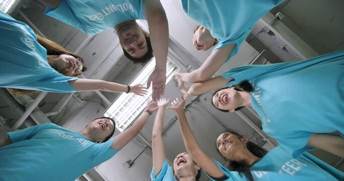Low angle close-up shot group of diverse asian volunteers team in blue t-shirts stack hands put palms together as unity and teamwork in slow motion. Social support and donation concept.