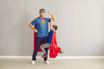 Happy strong young dad and active little child dressed as superheroes having fun at home. Father...