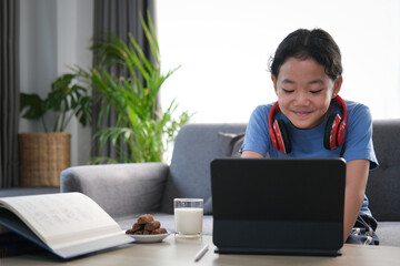 Cheerful young asian woman smiling and surfing internet on computer tablet in living room.