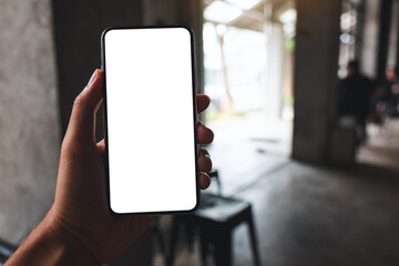 Mockup image of a man holding black mobile phone with blank white screen in cafe