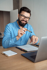 Young man happy positive smile speak to laptop camera sit at home office desk