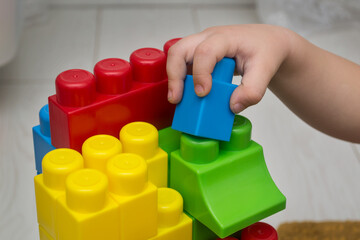 A child's hand builds a house from a constructor. Plastic colored blocks.