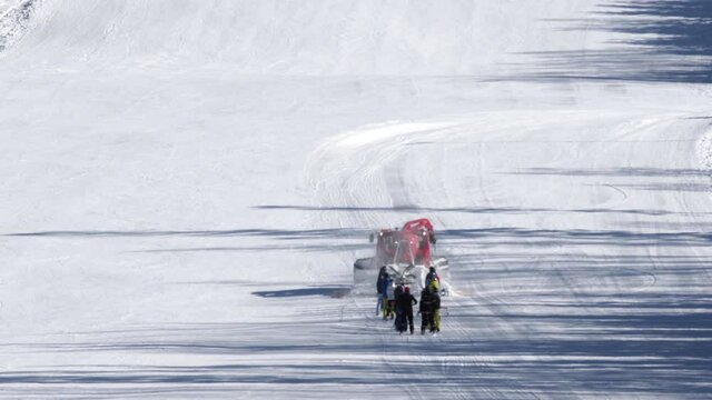 Red snow groomer towing a group of skiers on a snowy ski slope,Czechia.