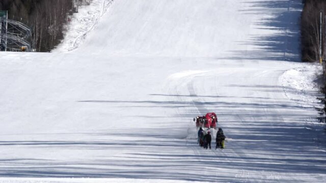 Red snow groomer towing a group of skiers up a snowy ski slope,Czechia.
