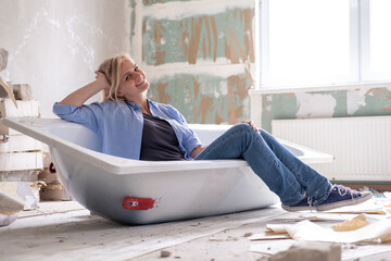 Renovation apartment. Creative story young happy woman sits in bathtub in the middle of the room....