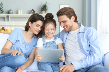 Positive friendly parents with smiling little daughter sitting on sofa together answering video call on digital tablet.