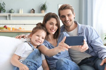 Beautiful young family with little child taking a selfie with a smartphone at home on the couch.