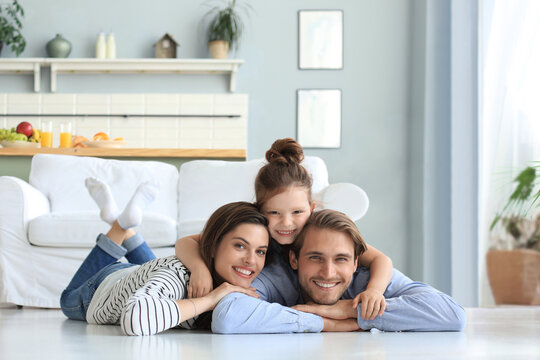 Young Caucasian family with small daughter pose relax on floor in living room, smiling girl kid hug embrace parents.