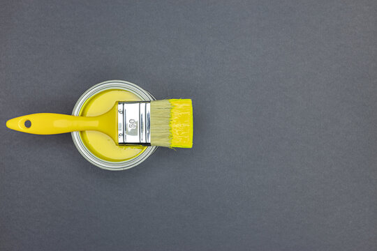 Paintbrush And Can Of Yellow Paint On Grey Background. House Renovation Concept. Top View.