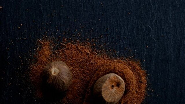 Nutmeg. Whole nutmeg and ground nutmeg in a wooden spoon on a black slate background