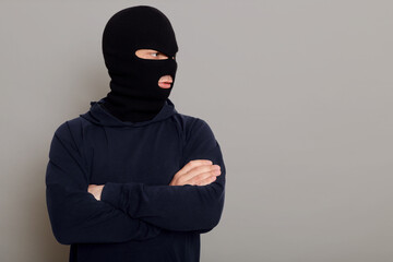 A criminal man in bandit mask and a black hoodie stands with folded hands on his chest, looking to...
