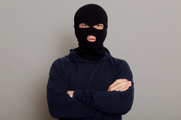 Self-confident criminal male posing isolated on a gray background, wearing a black hoodie and a...