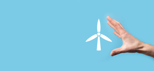 Hand holding an icon of a windmill that produces environmental energy on blue background.