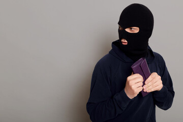 Frightened guy thief dressed in a black hoodie, stole a wallet and runs away looking back, afraid...