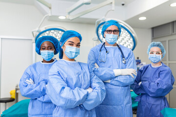 multi-ethnic group of four healthcare workers, a team of doctors, surgeons and nurses, performing surgery on a patient in a hospital operating room. They are looking at the camera.