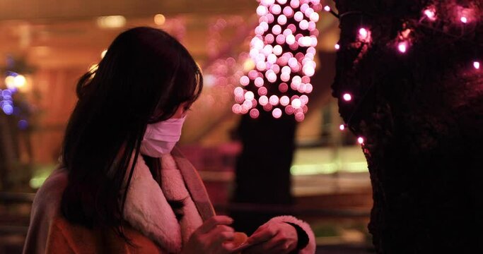 A Japanese mask woman shooting by smartphone at illuminated street closeup handheld