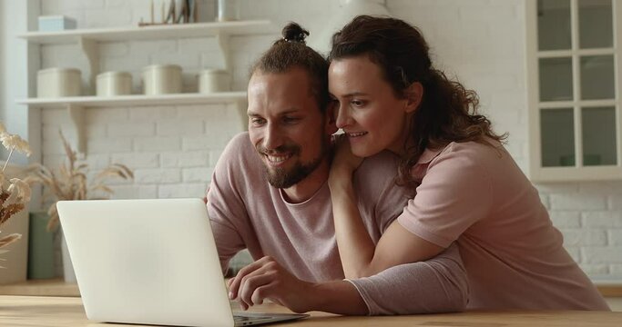 Happy bonding affectionate young couple looking at laptop screen, watching funny photo or videos, web surfing information planning vacation, choosing goods in online store, entertaining on weekend.